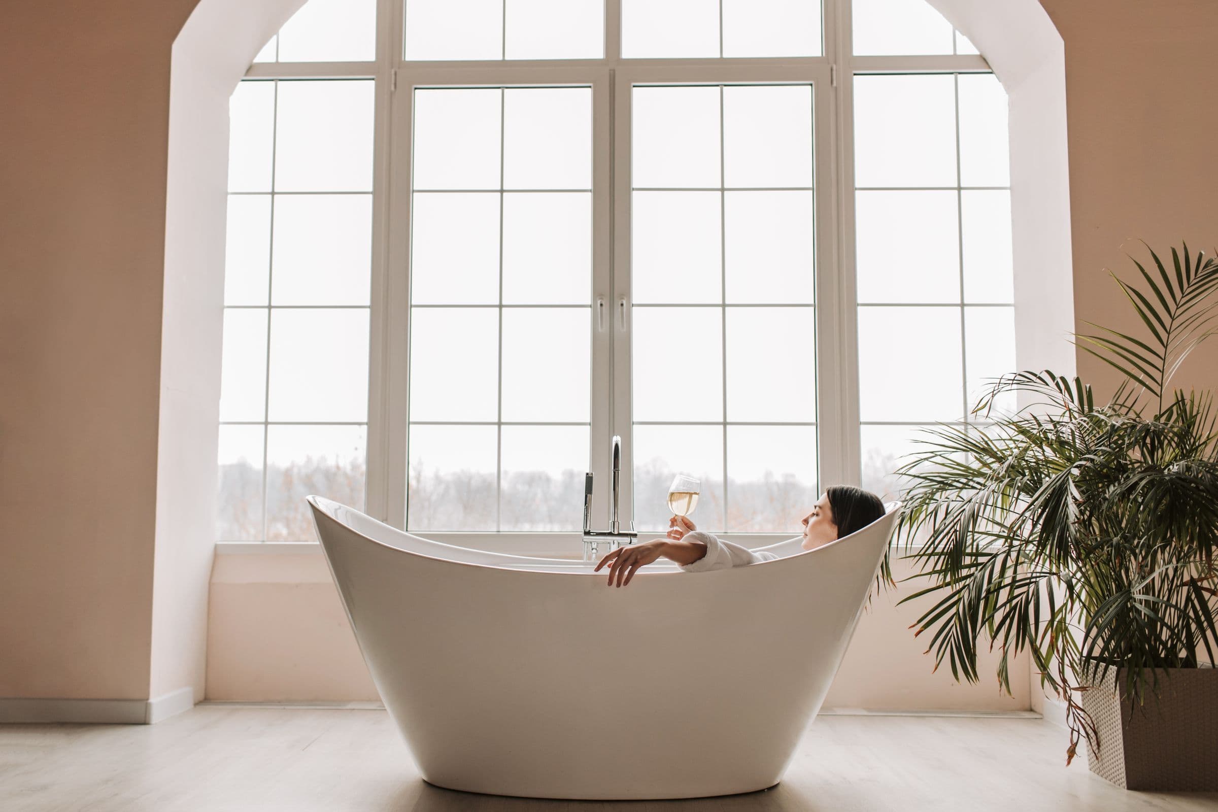 A freestanding bath in a bright room with tall windows